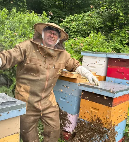 A man in brown suit standing next to beehives.