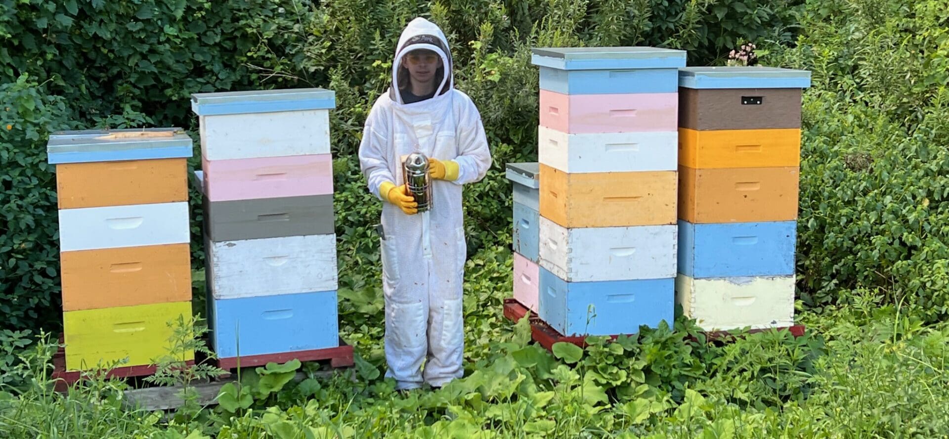 A man in white suit holding a bee hive.