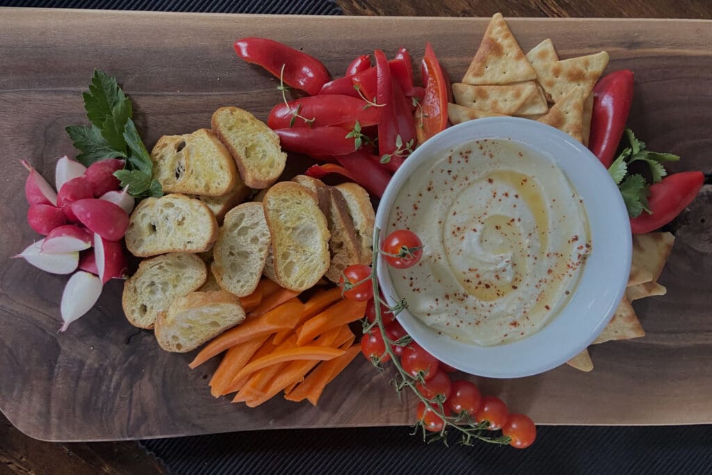 A wooden tray with crackers, bread and vegetables.